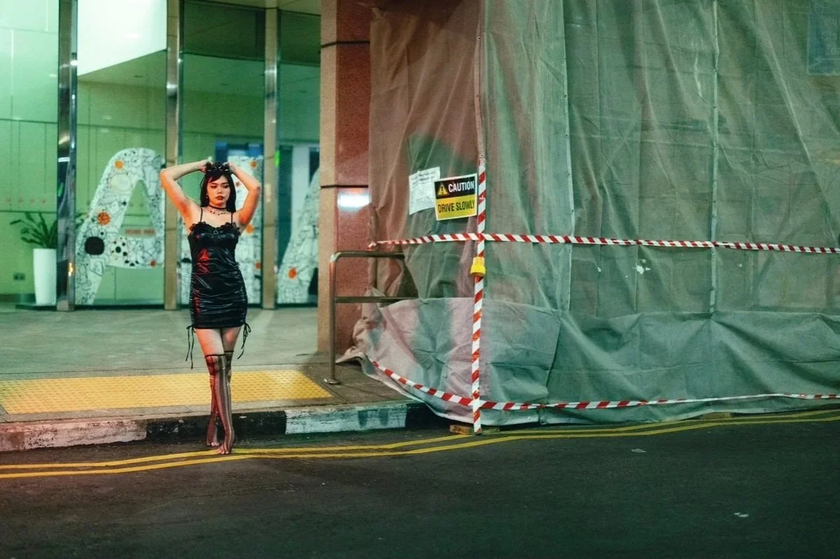 A woman in a black dress with red and black striped tights standing on sidewalk outside a building under construction, with caution tape and signs.