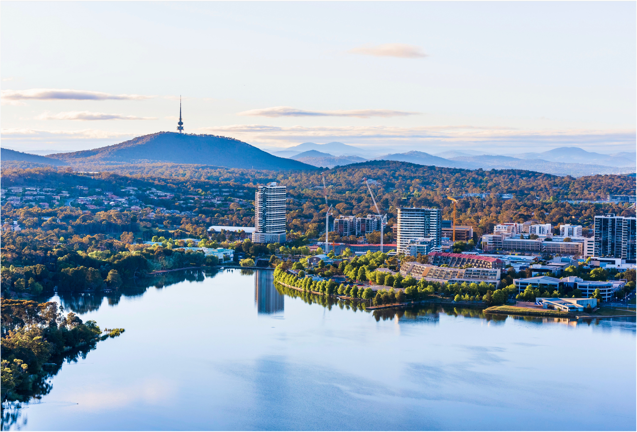 Wide angle photo of Canberra with a view city buildings by Lake Burley Griffin and Telstra Tower in the distance.