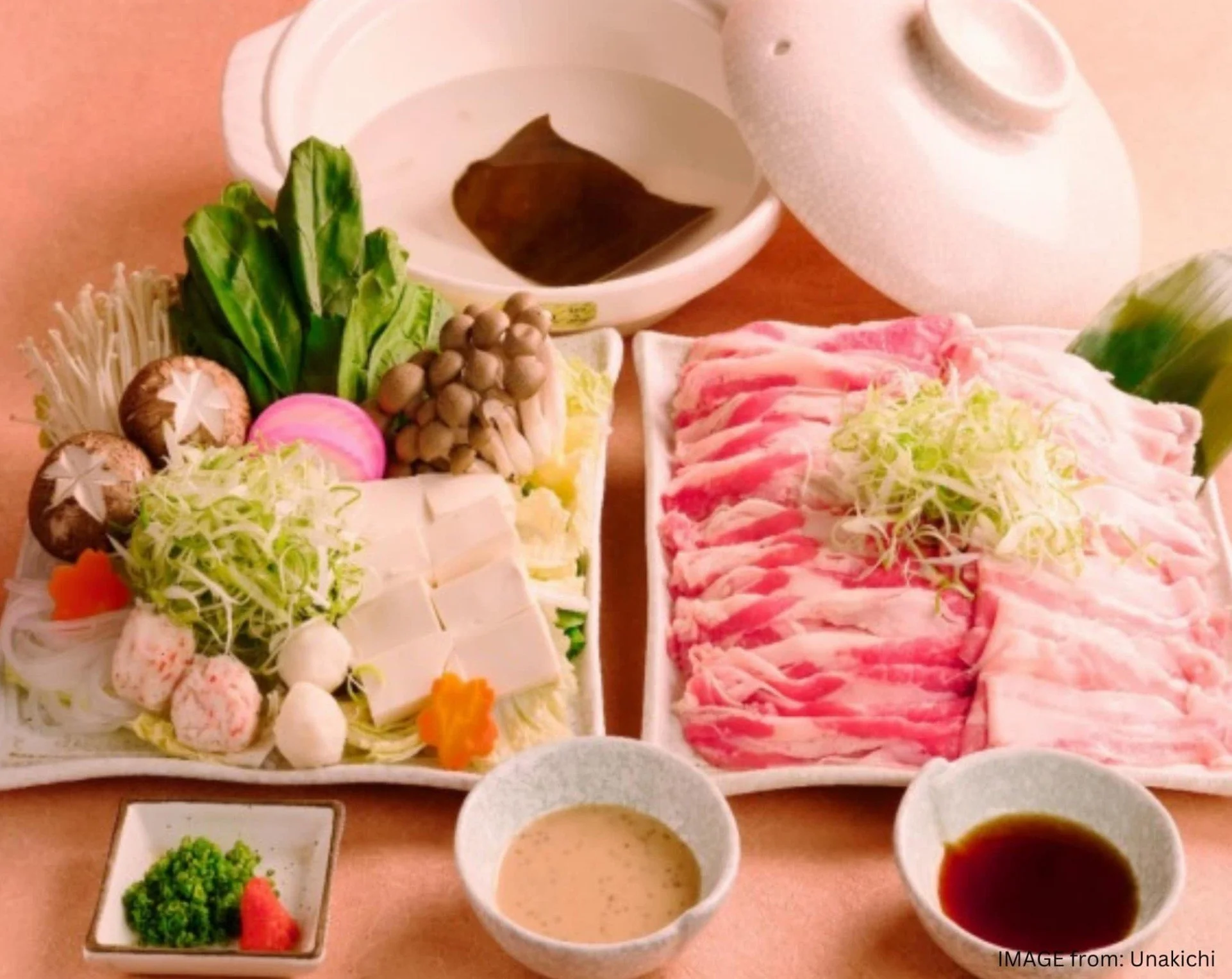 A sushi platter with vegetables, tofu, and sliced raw meat, accompanied by soy sauce, dipping sauces, and garnishes.