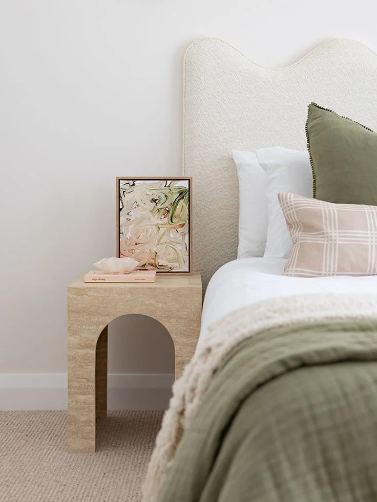 Bedroom with beige headboard, side table with abstract art, green and white bedding, and plaid pillow.