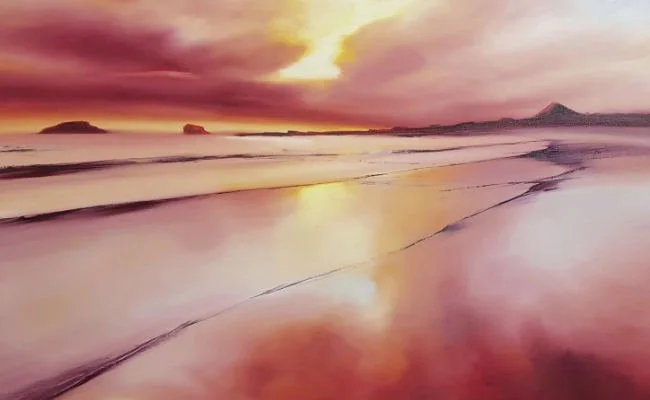 Colorful beach at sunset with pink, orange, and purple sky reflecting on wet sand and gentle waves.