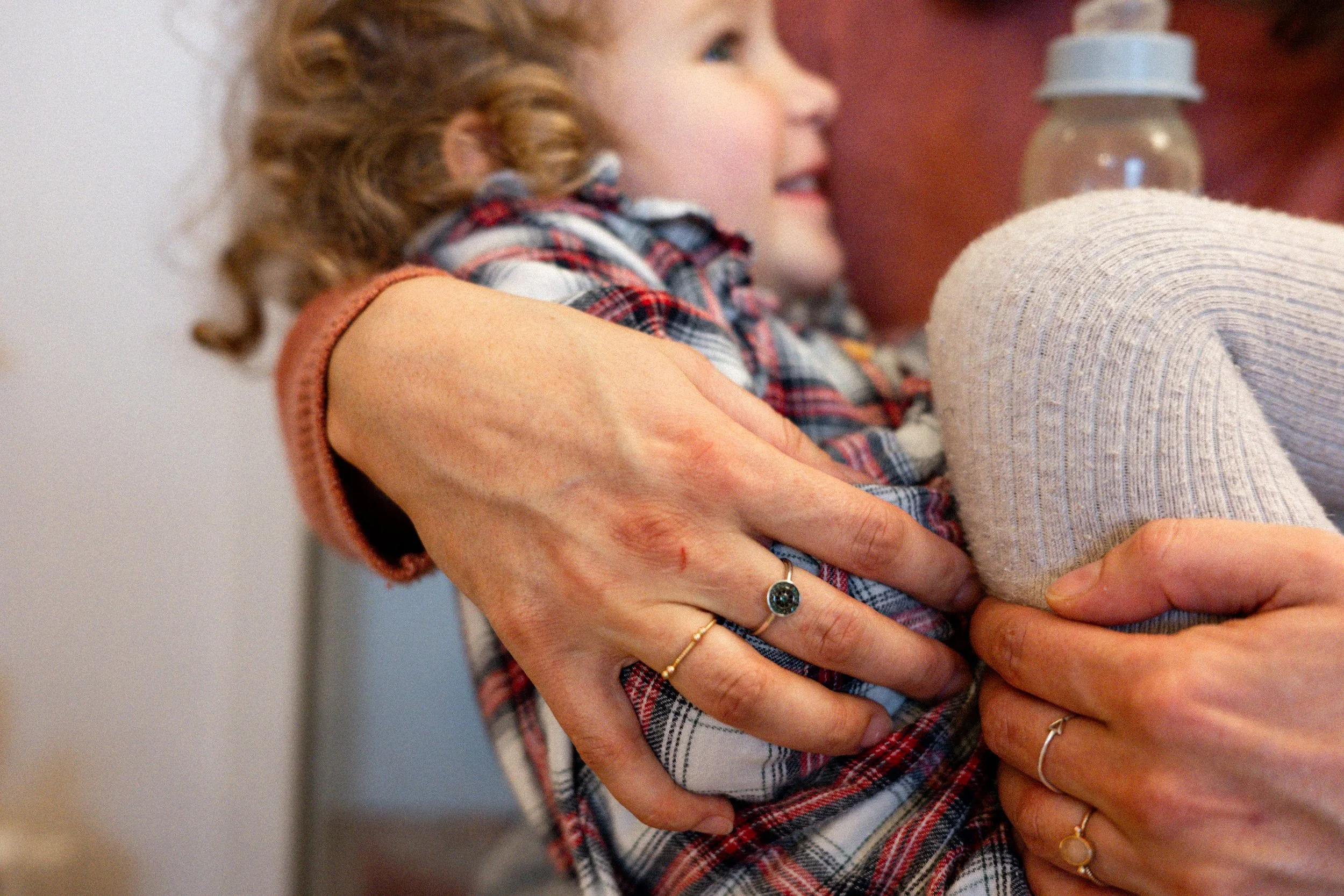 Eine junge Mädchen wird gestillt, gehalten von einer Person mit mehreren Ringen an den Fingern.