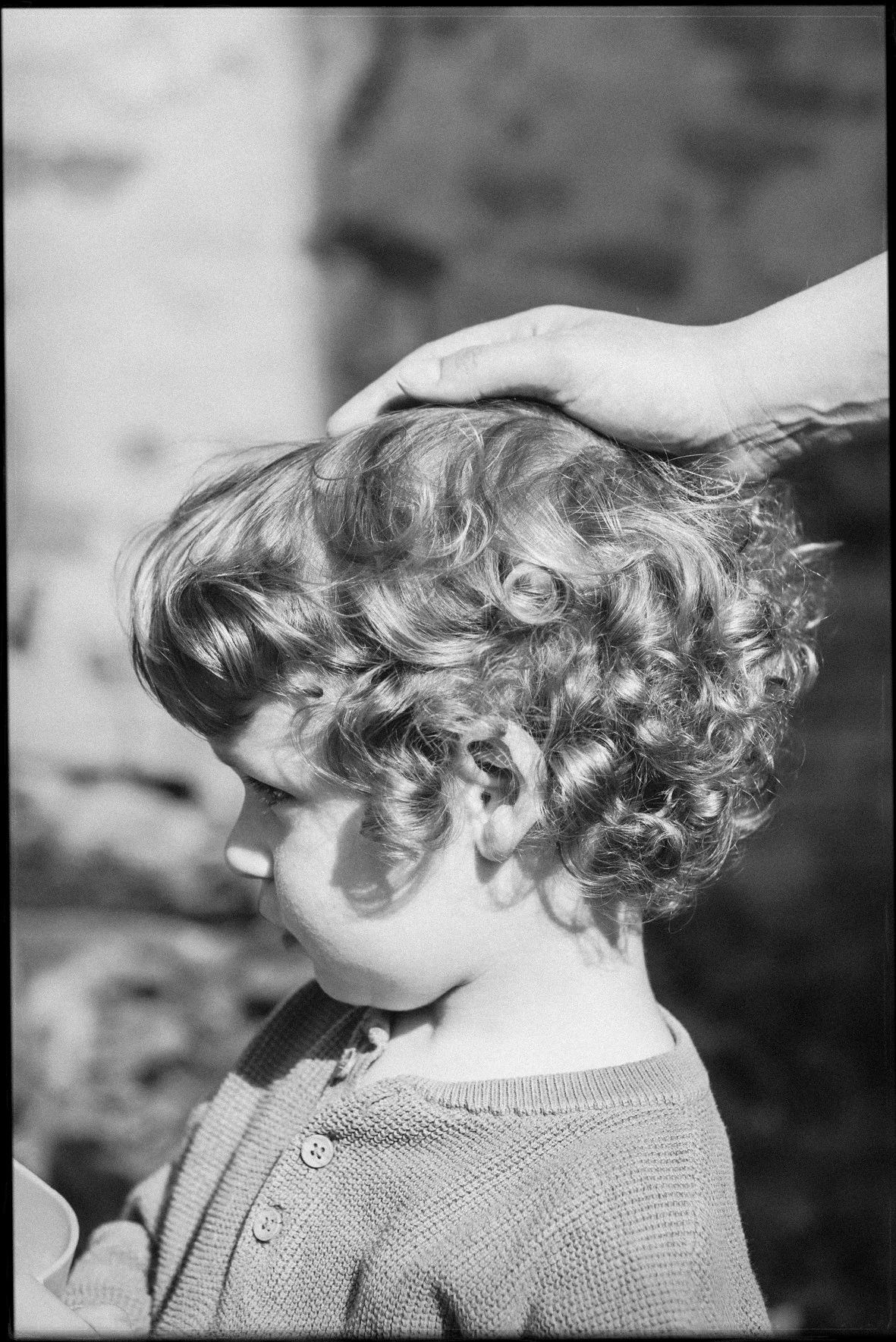 Ein Junge mit lockigem Haar wird von einer Hand berührt.