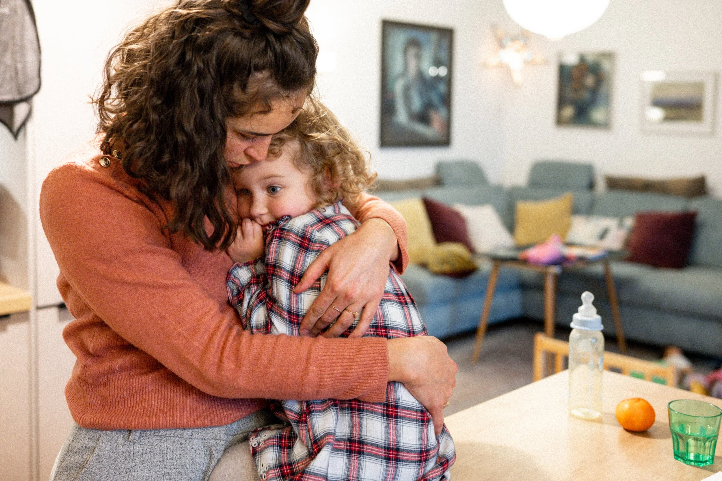 Eine Frau umarmt ein kleines Mädchen in einem Wohnzimmer.