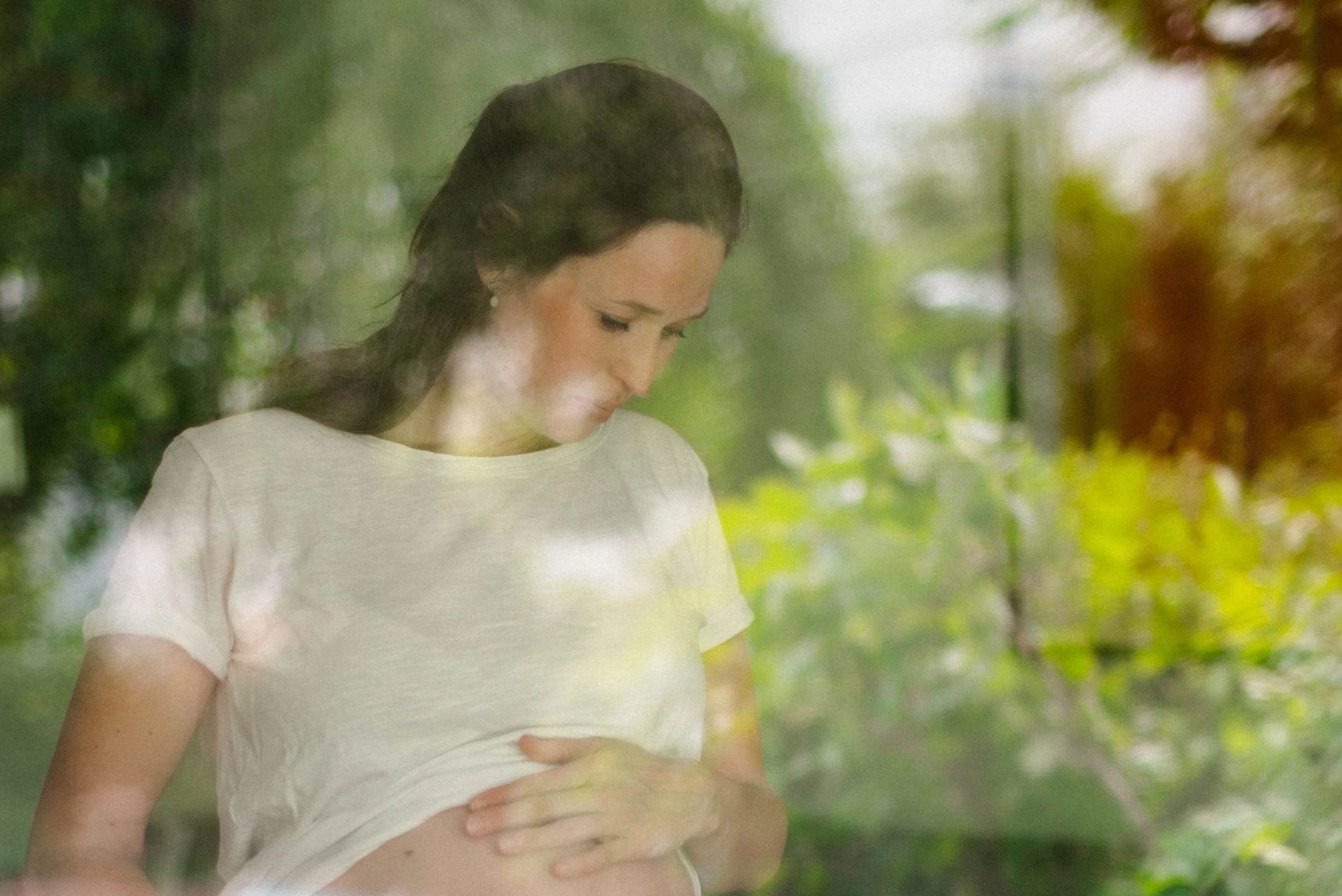 Eine Schwangere, die durch ein Fenster sieht, während sie ihre Hand auf den Bauch legt, Schwangerschaft.