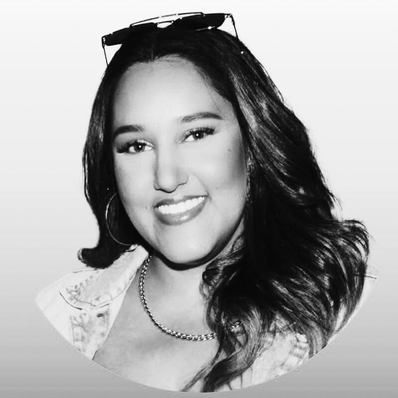 Black and white portrait of a woman with long hair, hoop earrings, necklace, and sunglasses on head, smiling.