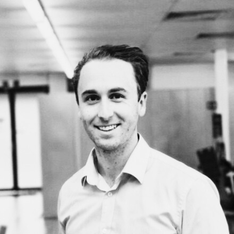 Black and white photo of a smiling person in a shirt standing indoors.