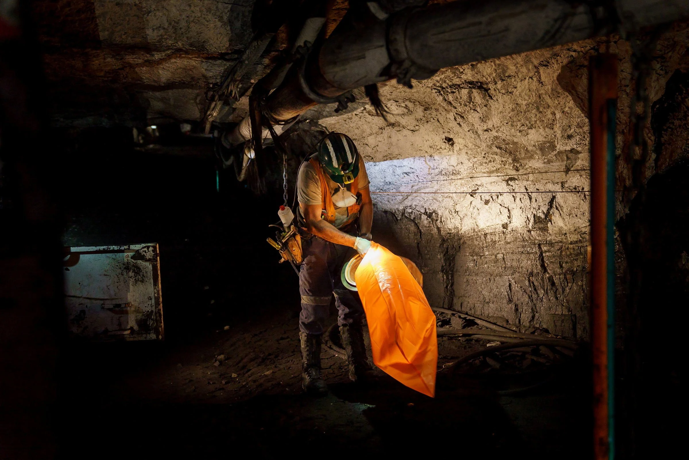 Underground mine worker inspecting equipment in a low-light working area at Myuna Mine in NSW.