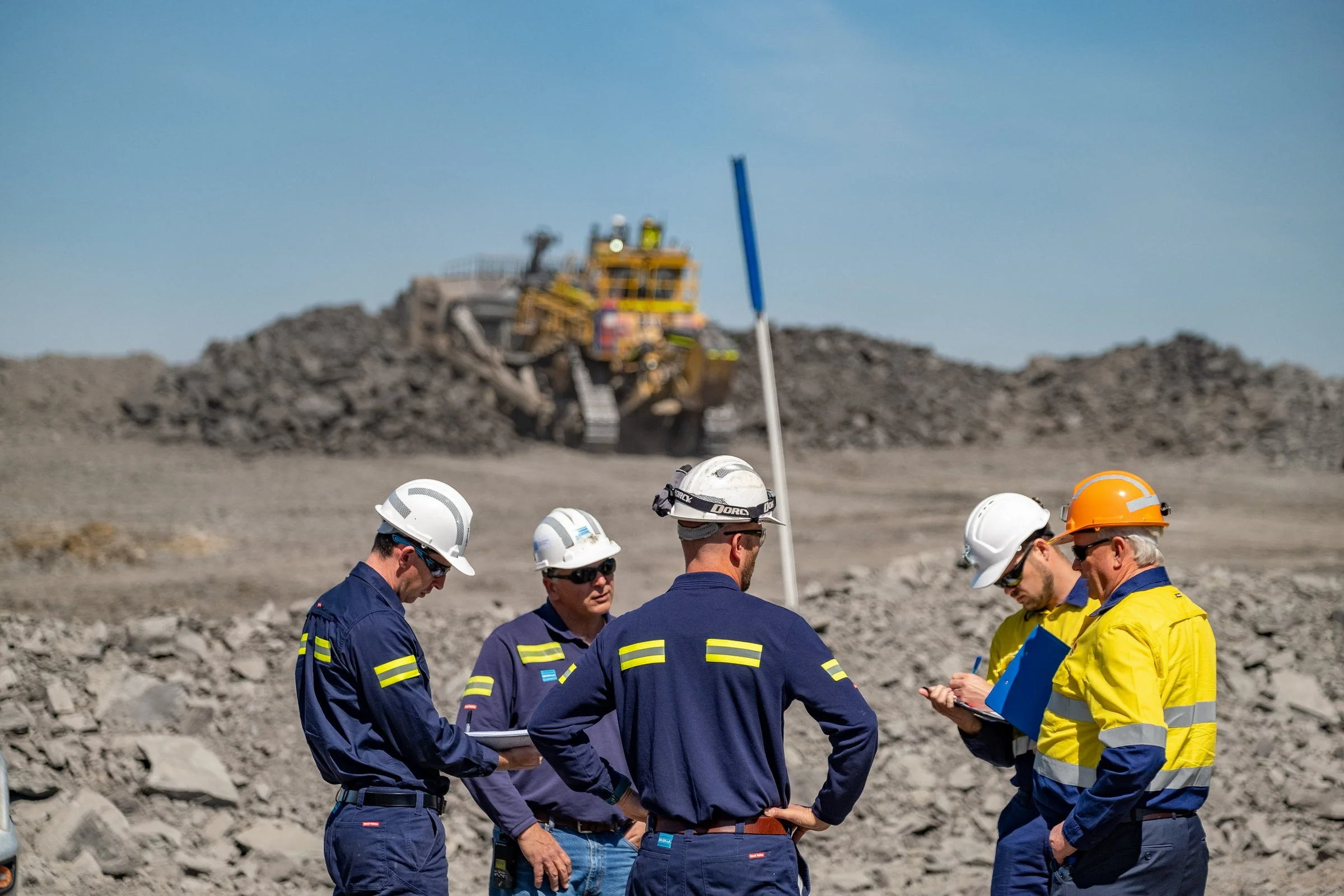 Mining inspectors and site personnel standing beside a light vehicle during an open-cut mine site visit in NSW.