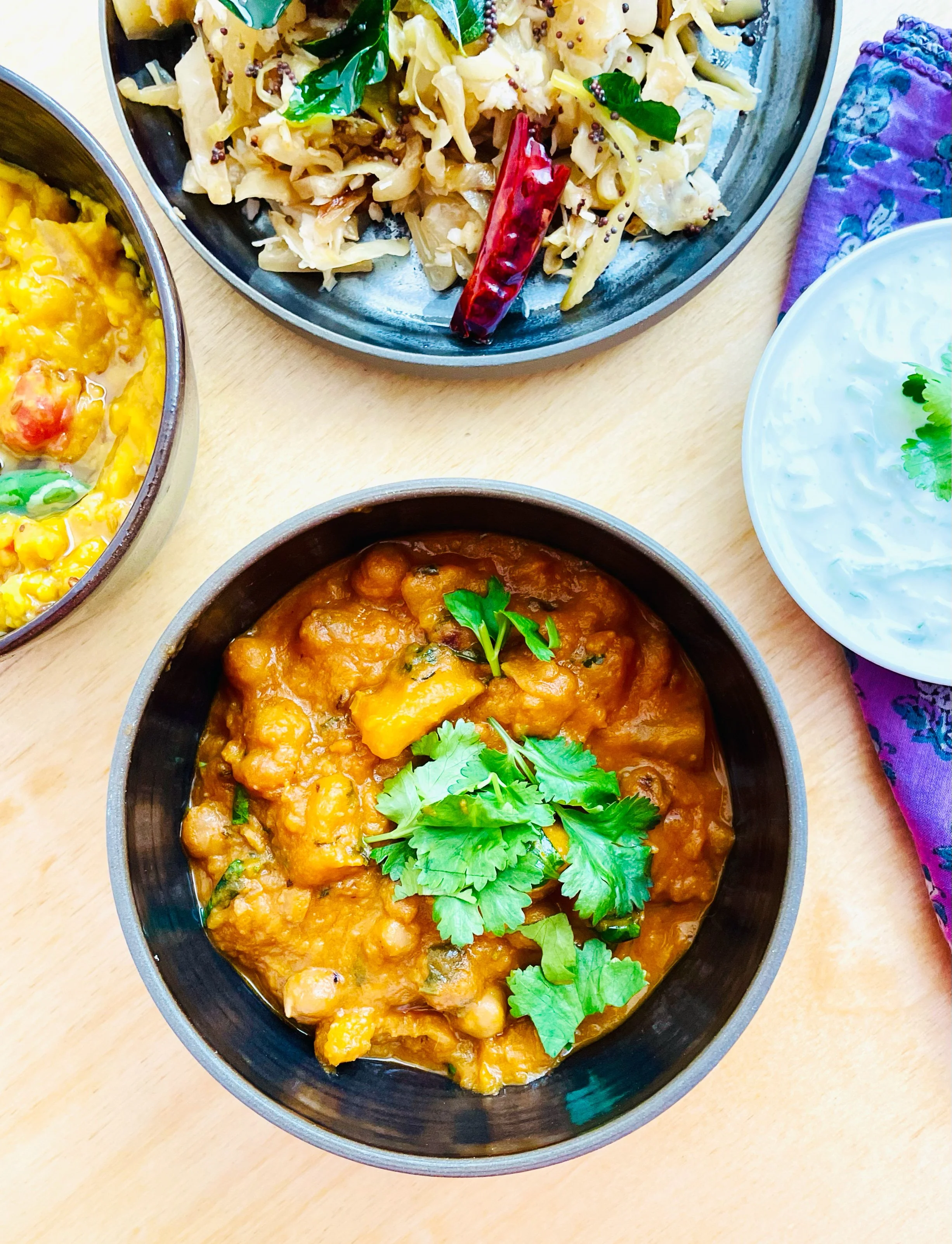 Schalen mit indischer vegetarischer Küche: Kichererbsencurry mit Koriander, Gemüsepfanne mit rotem Chili, gelbes Gemüsegericht und Joghurtsauce mit Kräutern