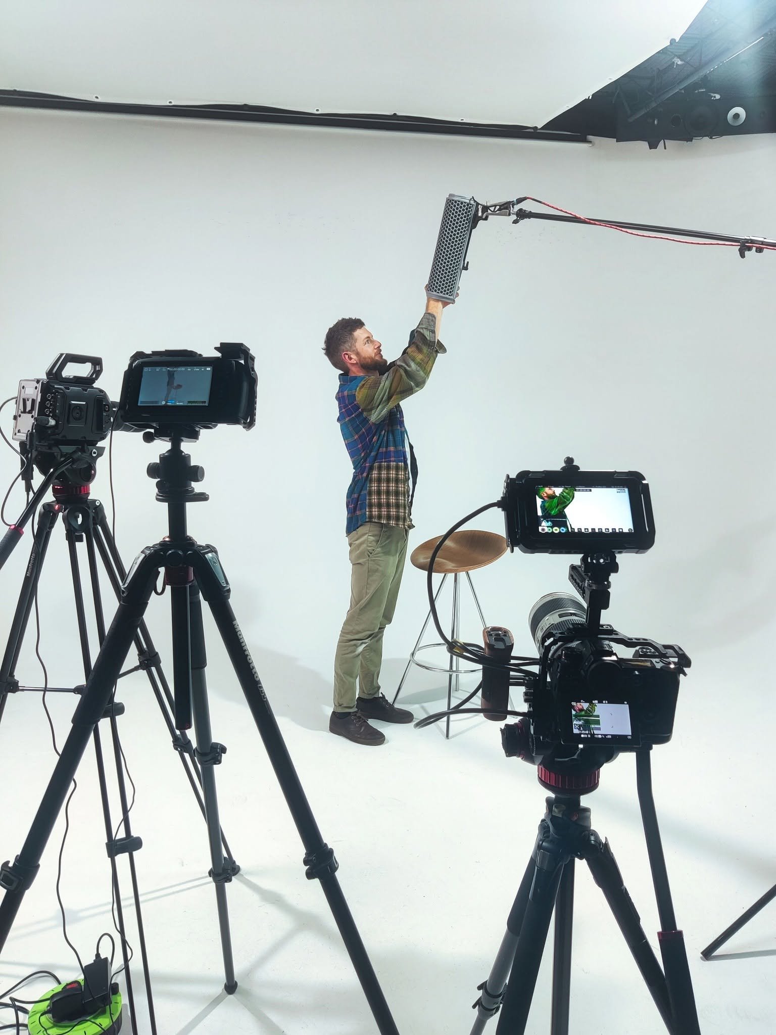Matt Paish adjusting a boom microphone in a white studio surrounded by video cameras.
