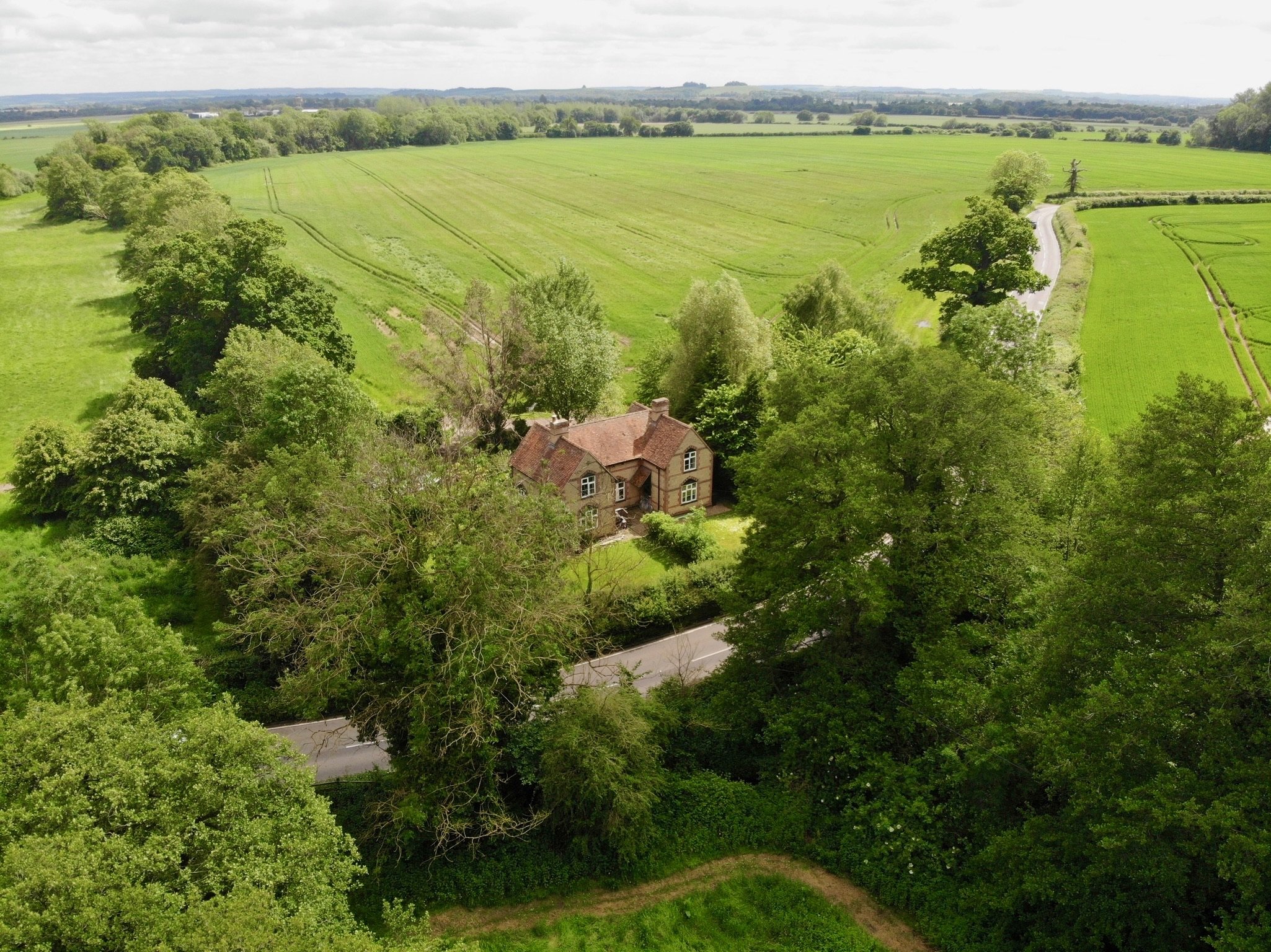 A house surrounded by trees in a rural landscape with green fields and a winding road.