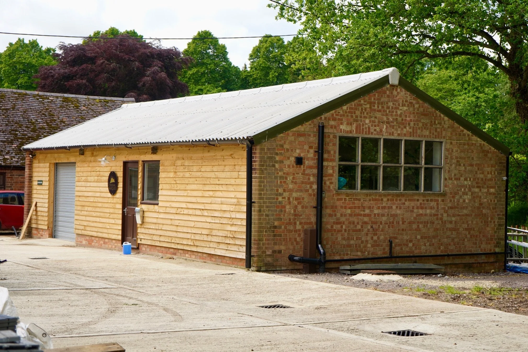 Wood-clad workshop building with metal roof and brick side wall.