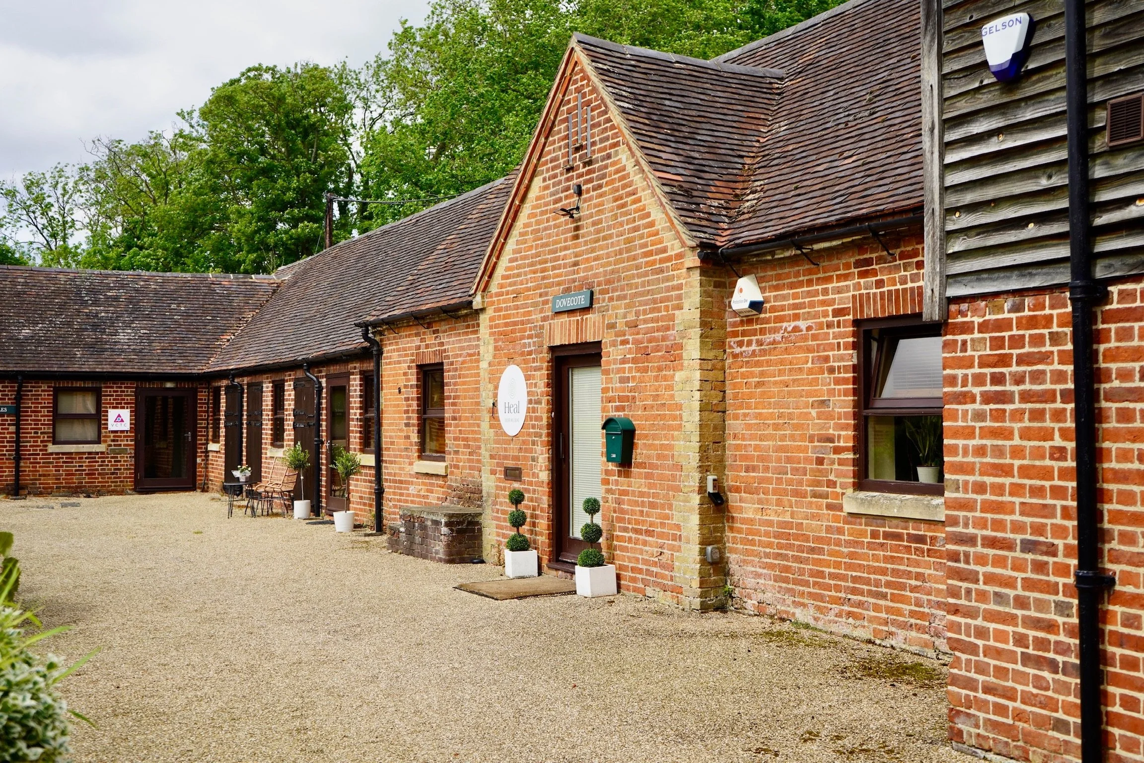 Brick building with pitched roof and courtyard, featuring signs reading "Dovecote" and "Ideal Collection."