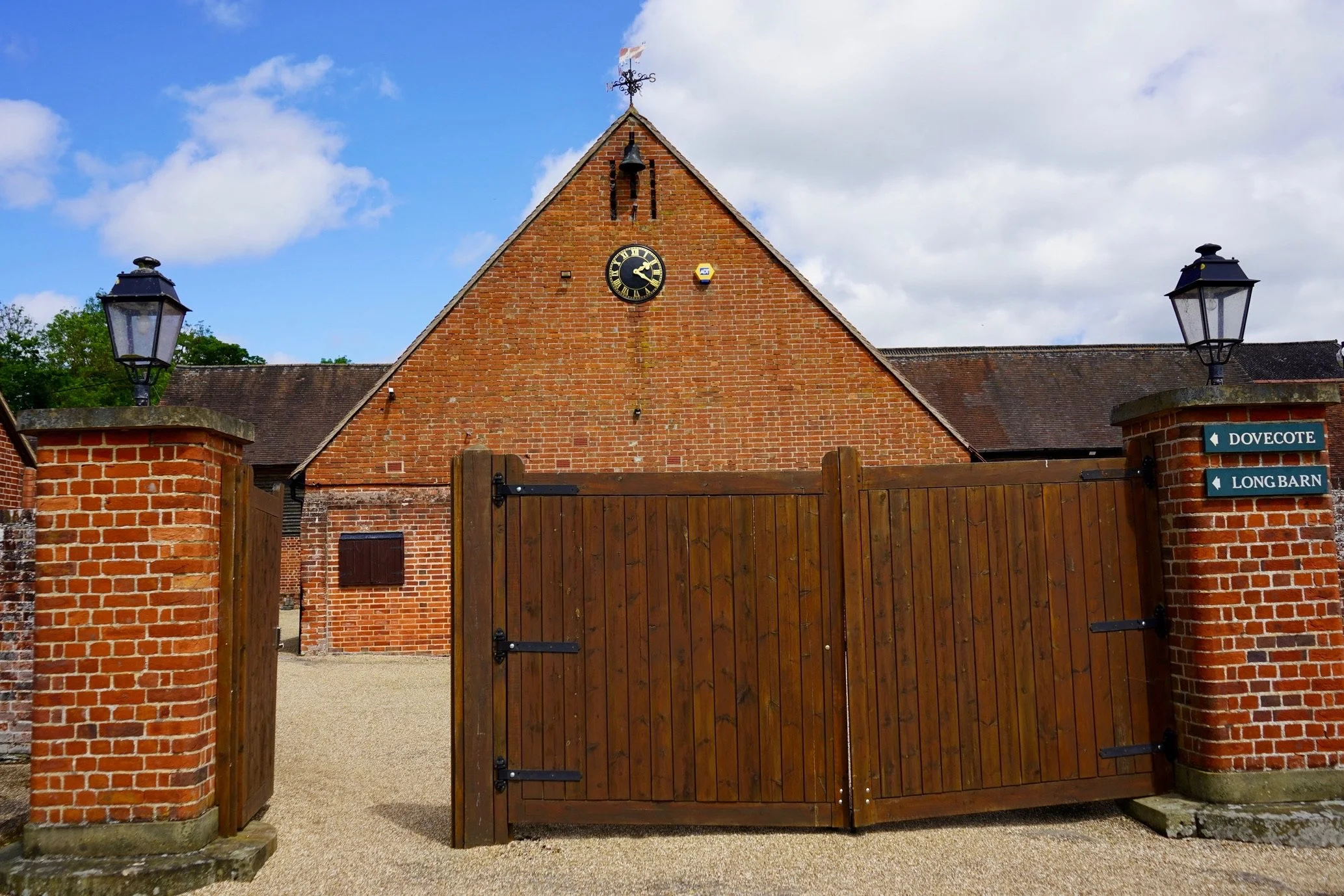 Wooden gate in front of a brick building with a clock and weather vane.