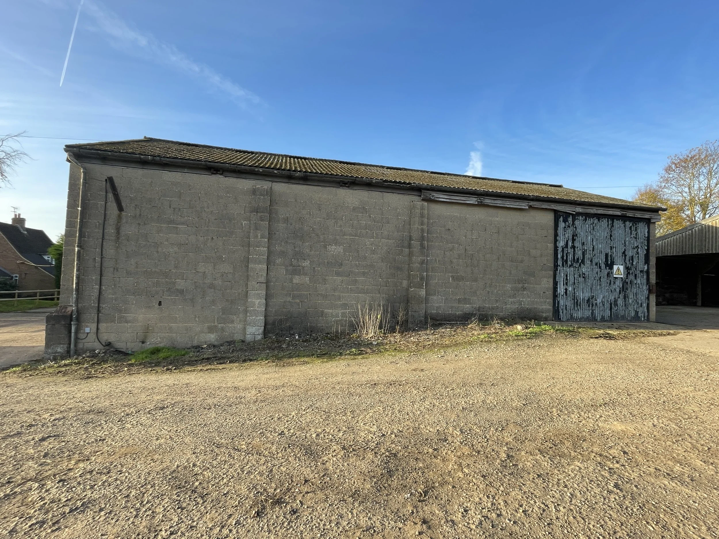 A weathered gray brick building with a large blue wooden door and a warning sign, set against a clear blue sky with a few wispy clouds.