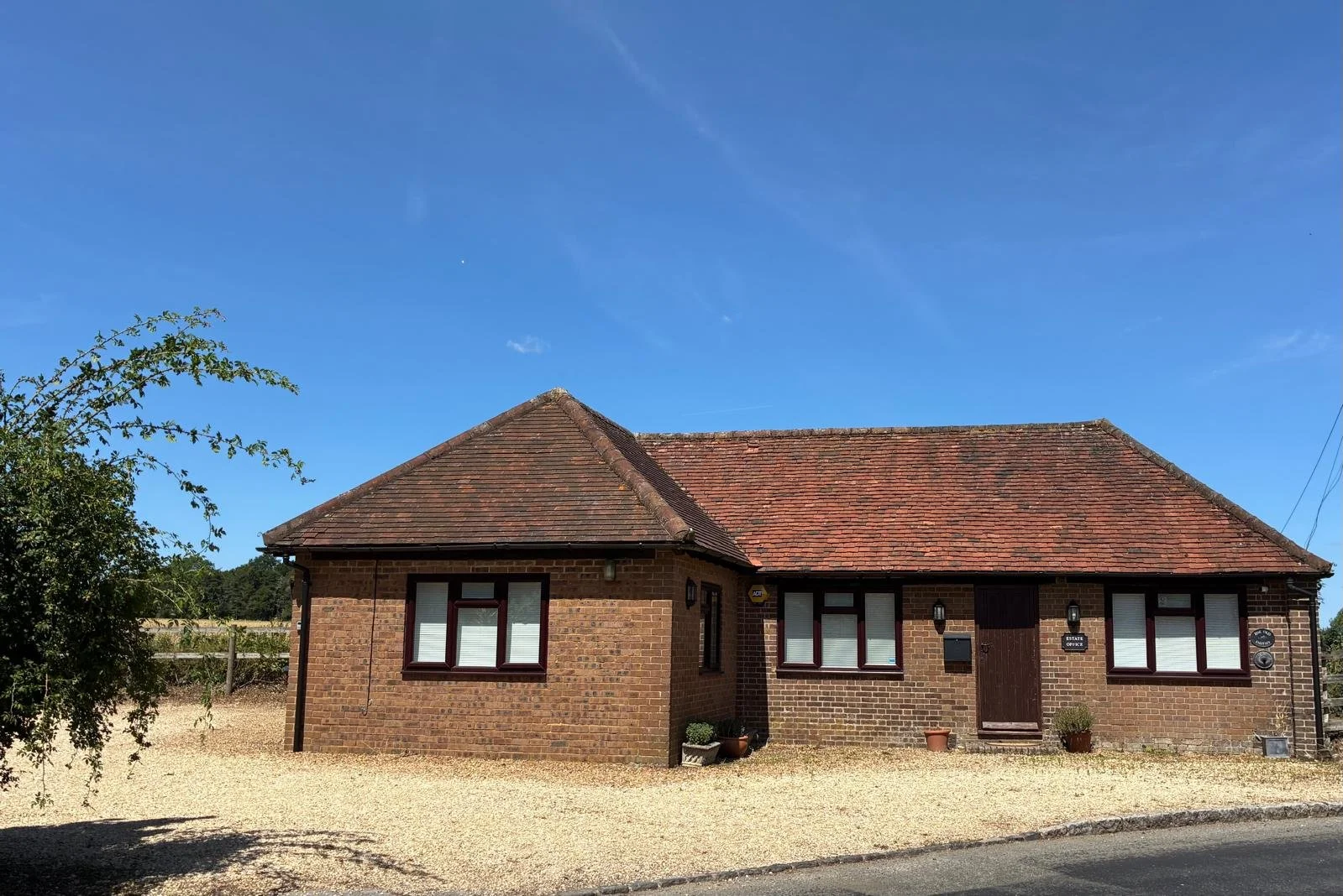 Brick house with a tiled roof under a blue sky, with windows and potted plants outside.