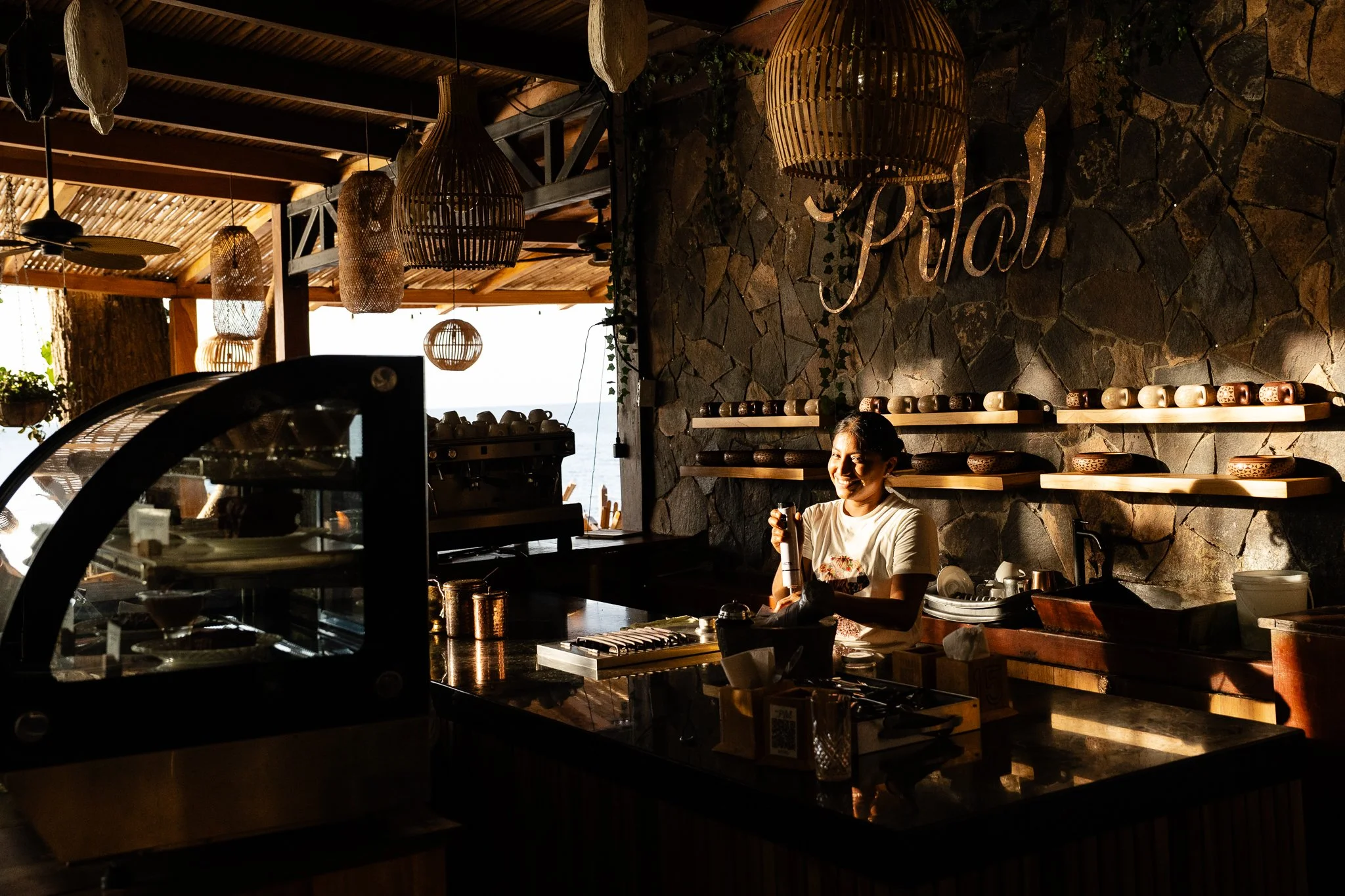 A woman smiling behind the bar of El Pital in warm late-afternoon light