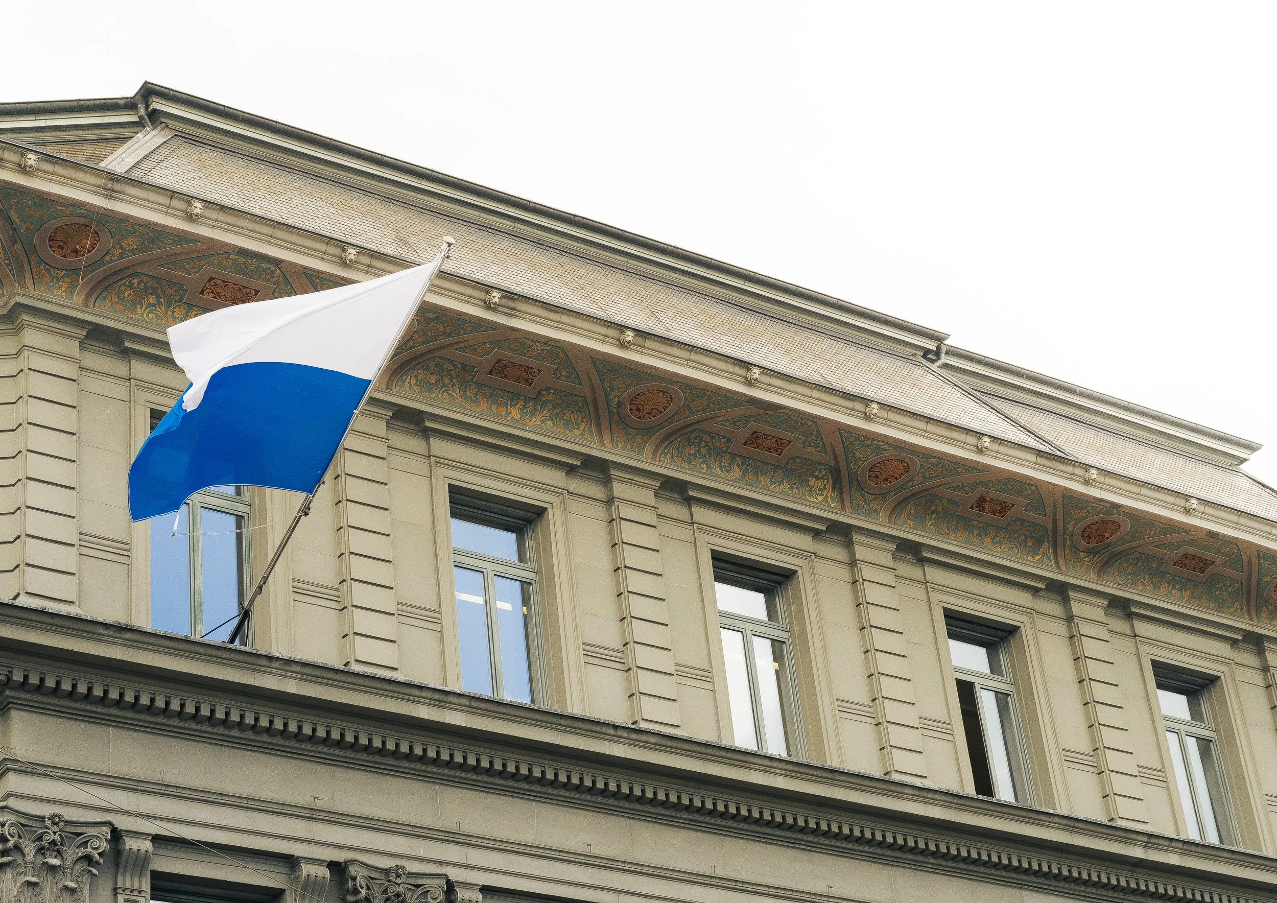 A building with ornate decorative architecture and a flagpole displaying the Russian flag, which has white, blue, and red horizontal stripes. post luzern. luzern. lucerne city