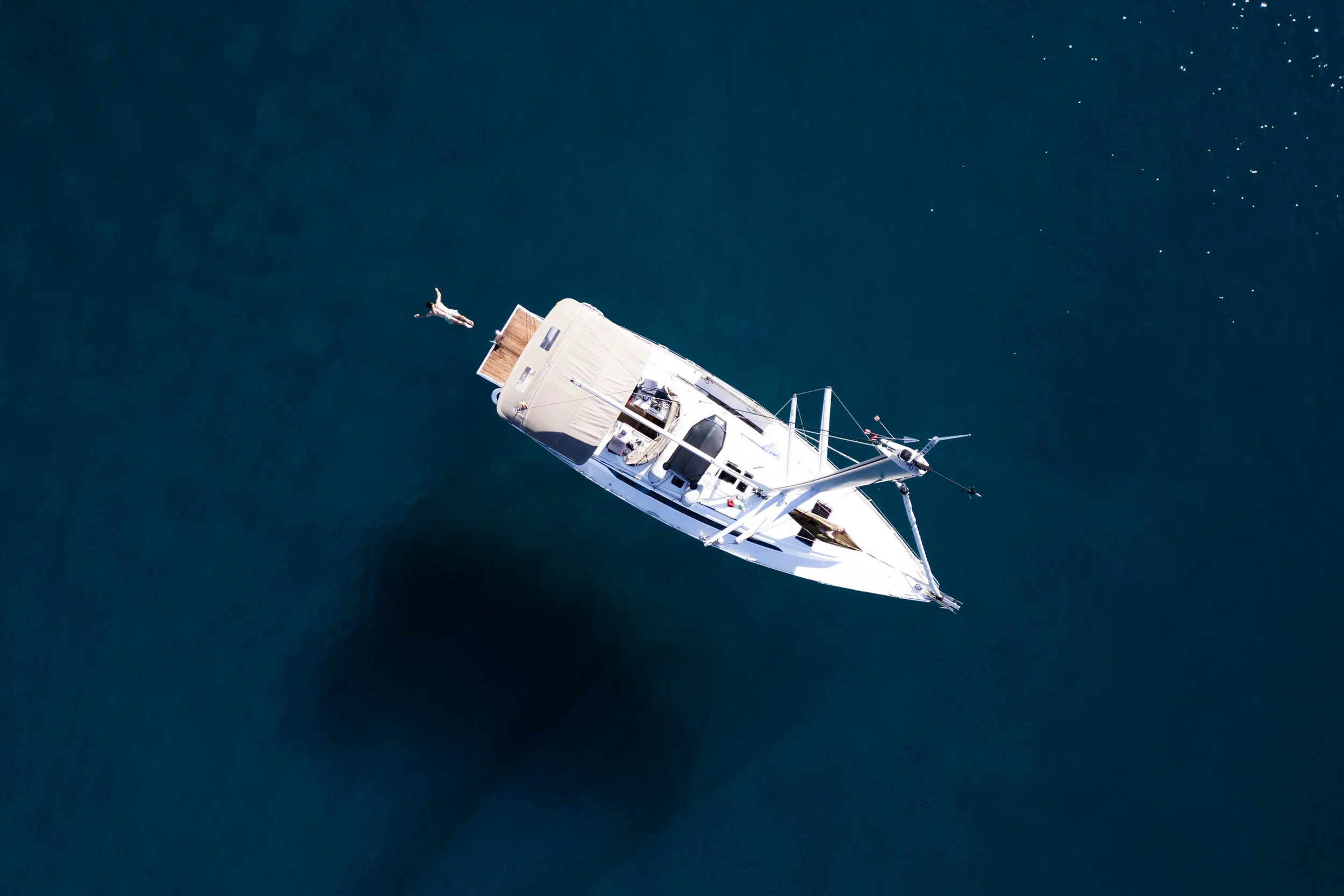 Aerial view of a sailboat on deep blue water with a swimmer beside it