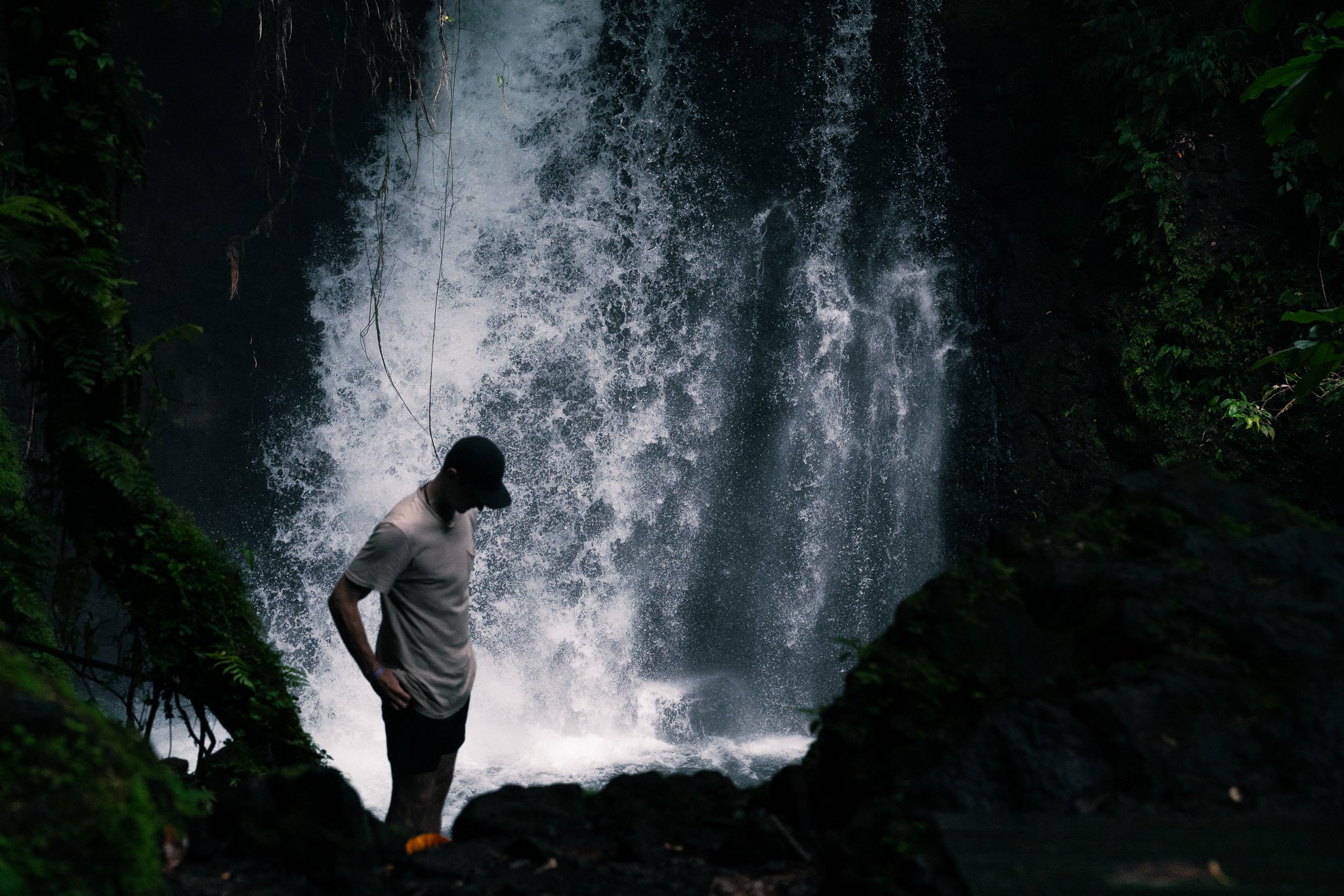 Person standing near a waterfall in a lush, green forest. fineart print. rainforest. flurin giebel. 