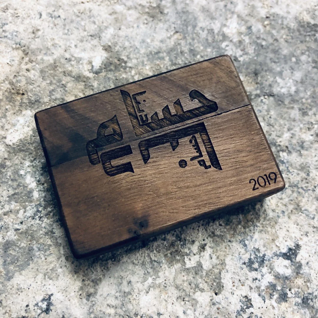 A small wooden jewellery box engraved with Arabic calligraphy and the year 2019, placed on a stone surface.