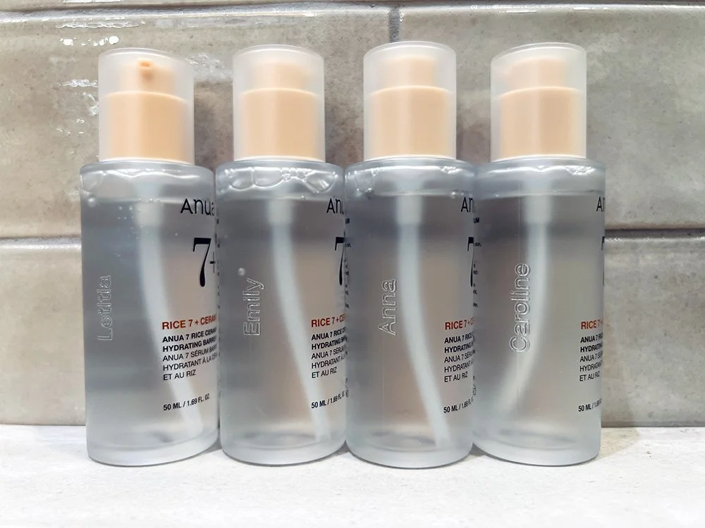 Four clear bottles of skincare serum with beige pump caps, that have been engraved.