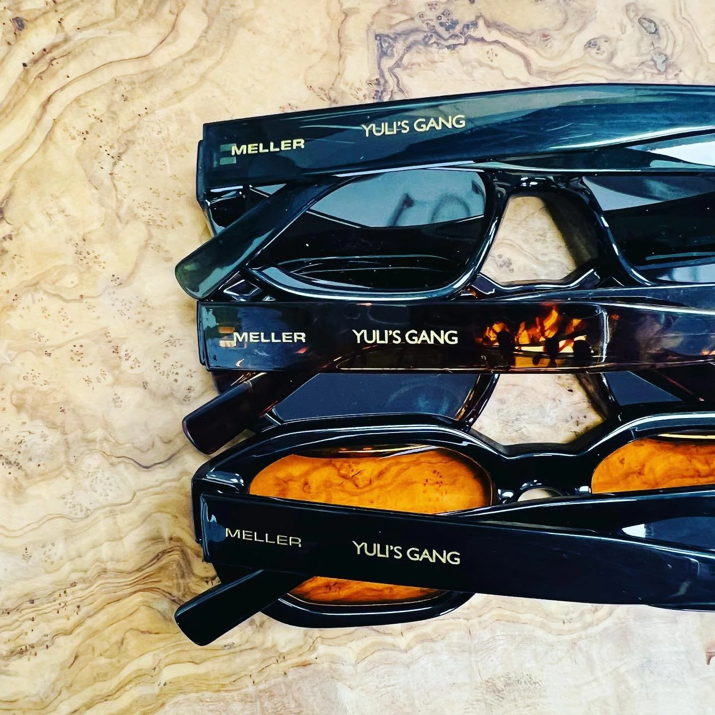 Four pairs of sunglasses stacked on a wooden surface, each pair engraved.