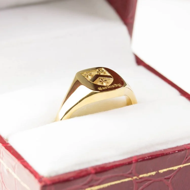 Gold signet ring engraved with a family coat of arms resting inside a red jewellery box with white interior padding.