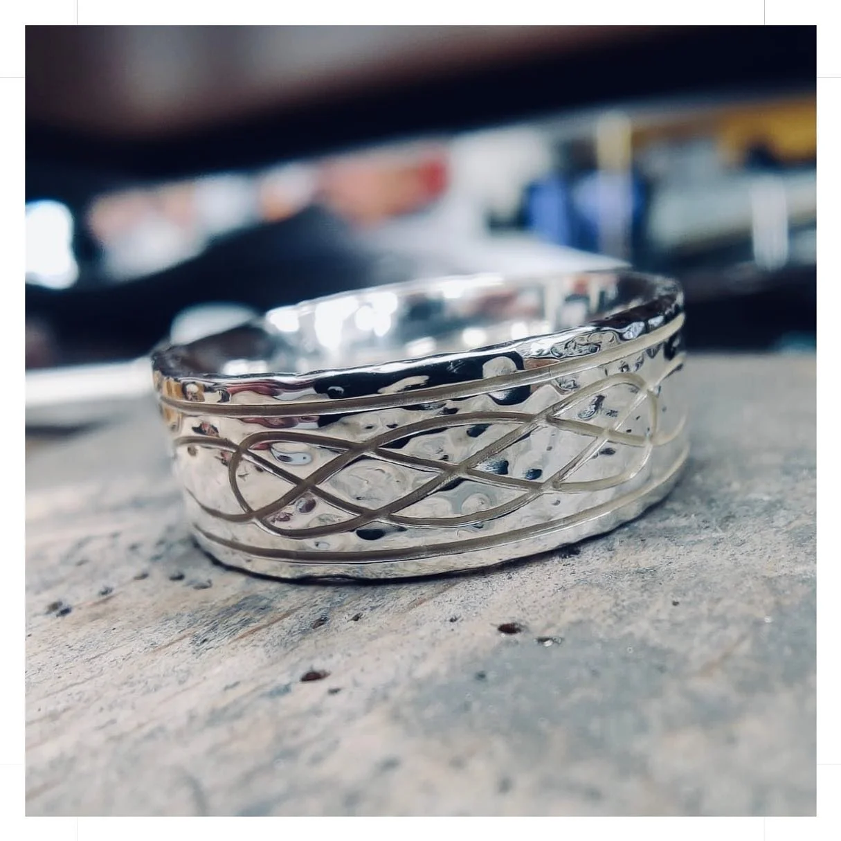 Silver ring engraved with a Celtic knot design resting on a jeweller's bench.