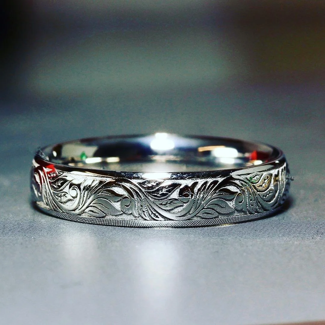 Close-up of a silver ring with intricate engraved floral and vine patterns resting on a gray surface.