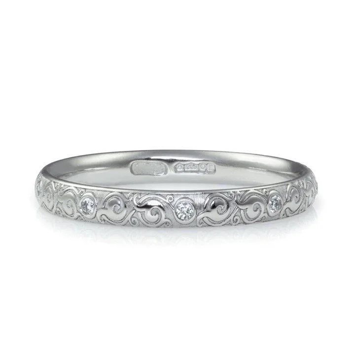 Silver ring engraved with ornate swirls and with small diamonds embedded.