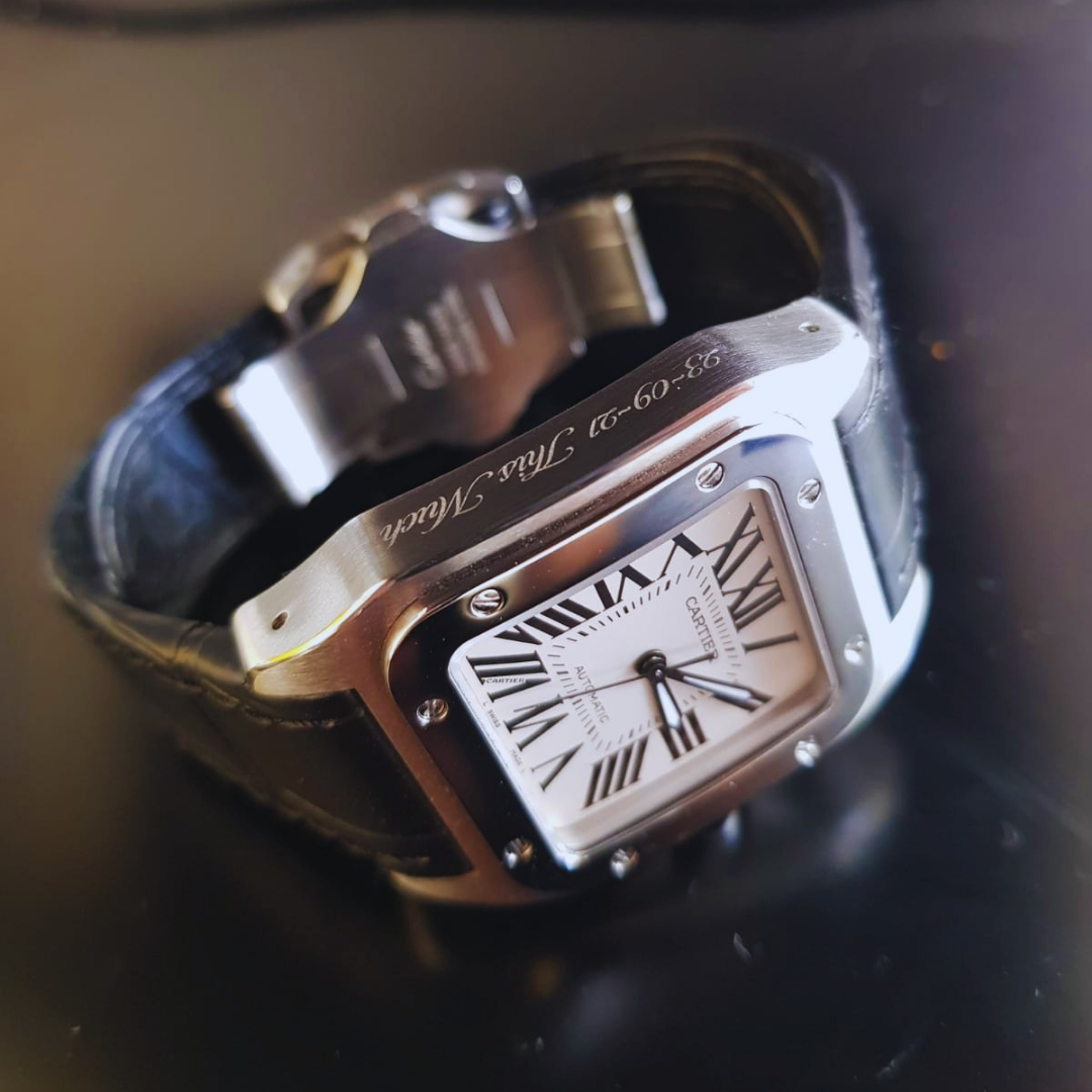 Close-up of an engraved Cartier watch with a black leather strap, silver case, and white dial featuring Roman numerals and black hands.