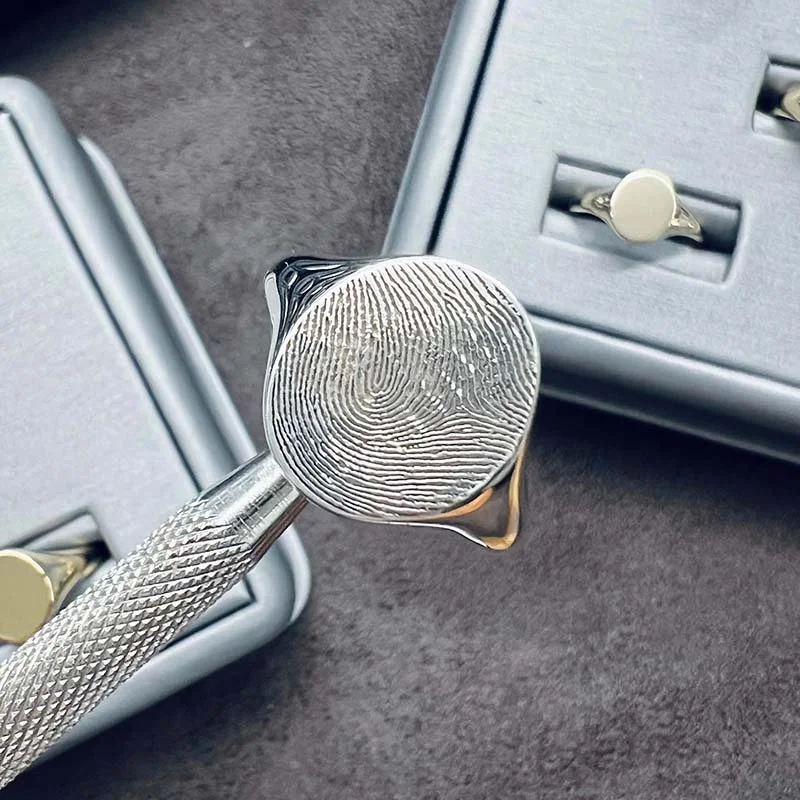 A silver signet ring engraved with a fingerprint.
