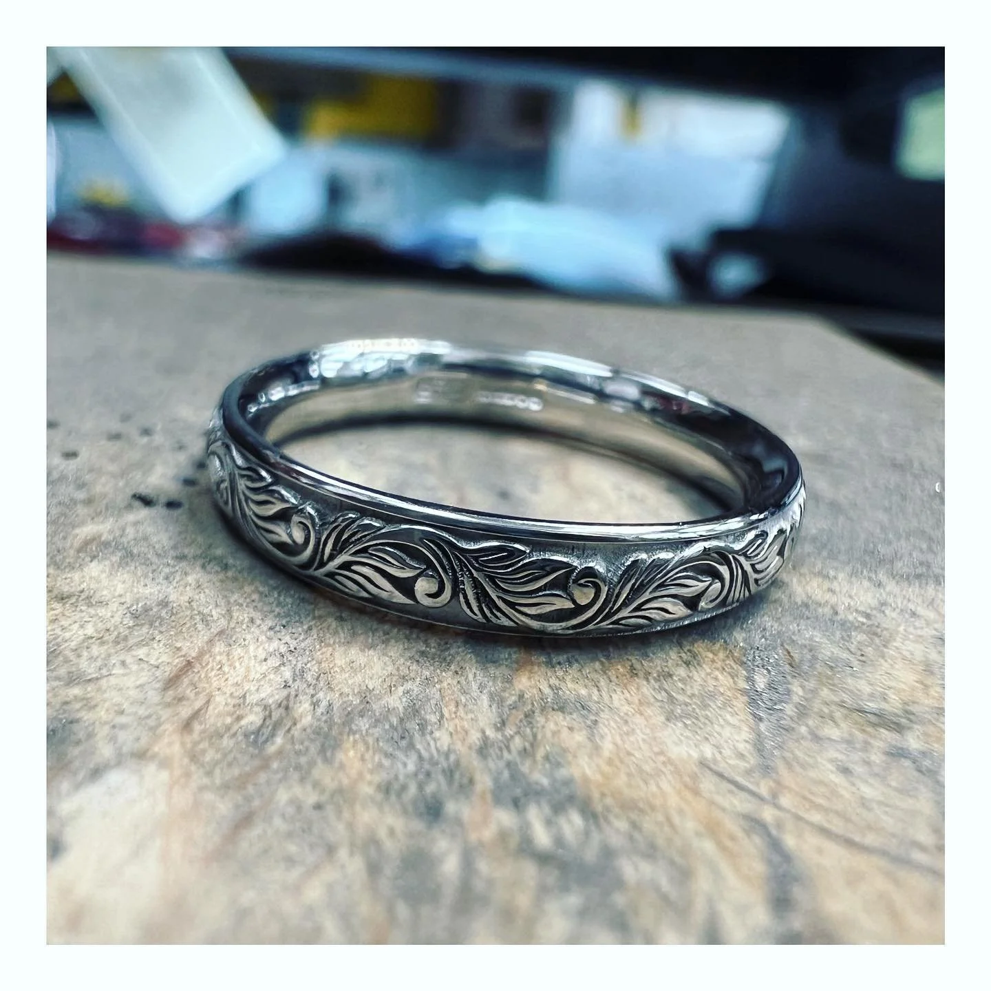 Close-up of a silver ring with an intricate, engraved, swirling leaf-like pattern.