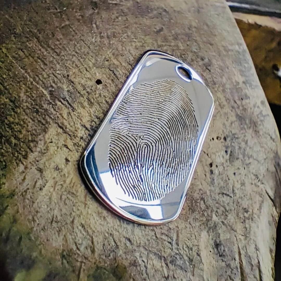 A silver tag engraved with a fingerprint resting on a jeweller's bench.