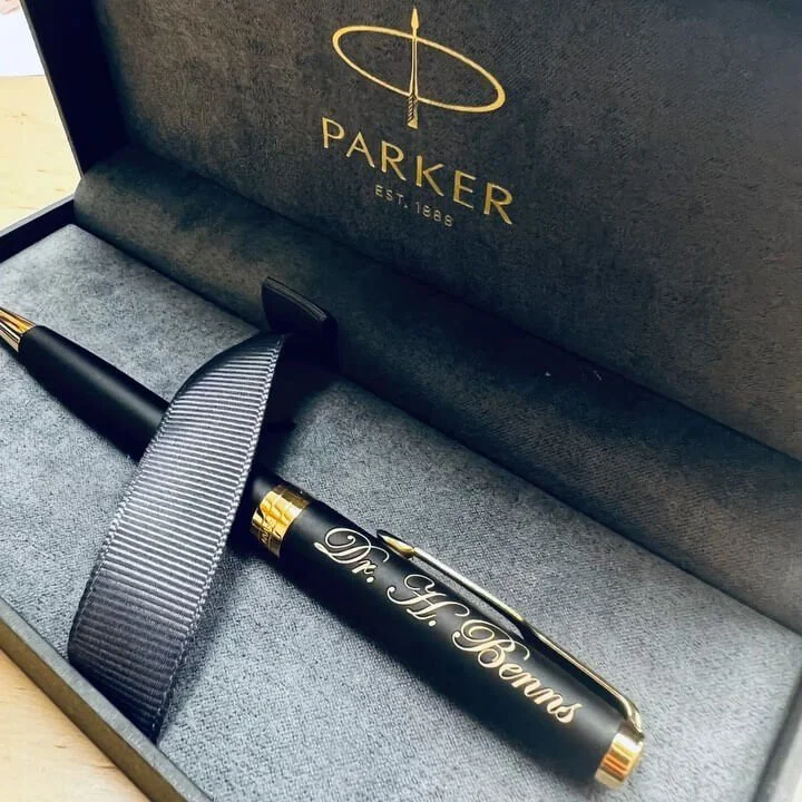 A black pen with gold accents and an engraved inscription inside a black gift box branded with the Parker logo.