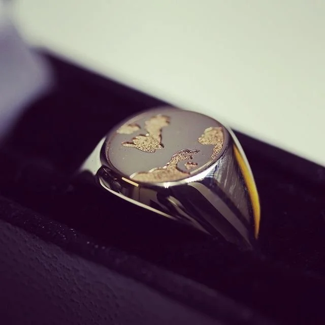 Close-up of a silver signet ring engraved with a map resting inside a black jewellery box