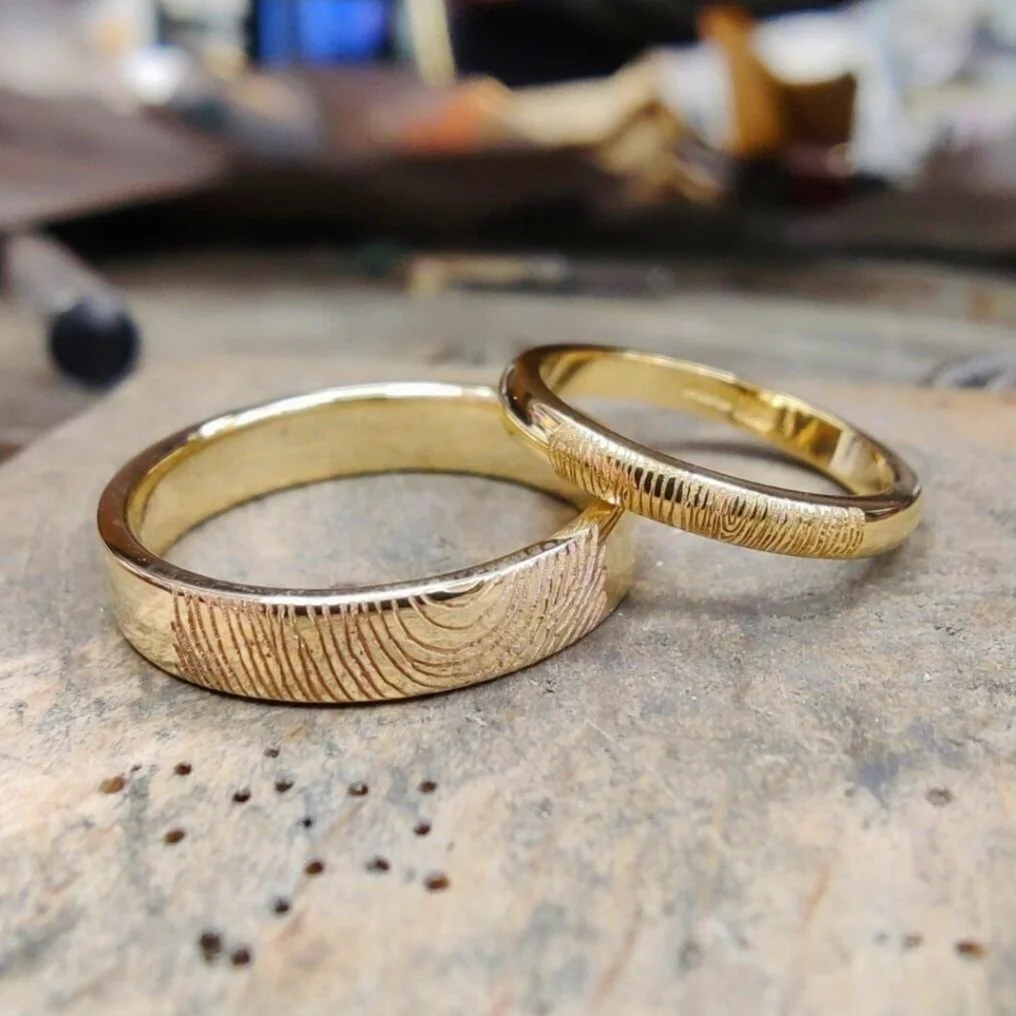 Two gold wedding bands with an engraved fingerprint on a jeweller's bench.