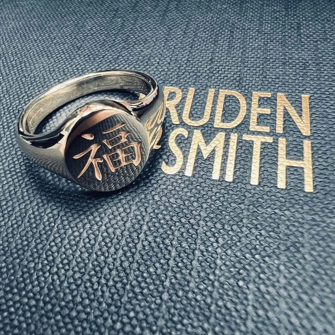 A silver signet engraved with Chinese characters, placed on a textured surface.