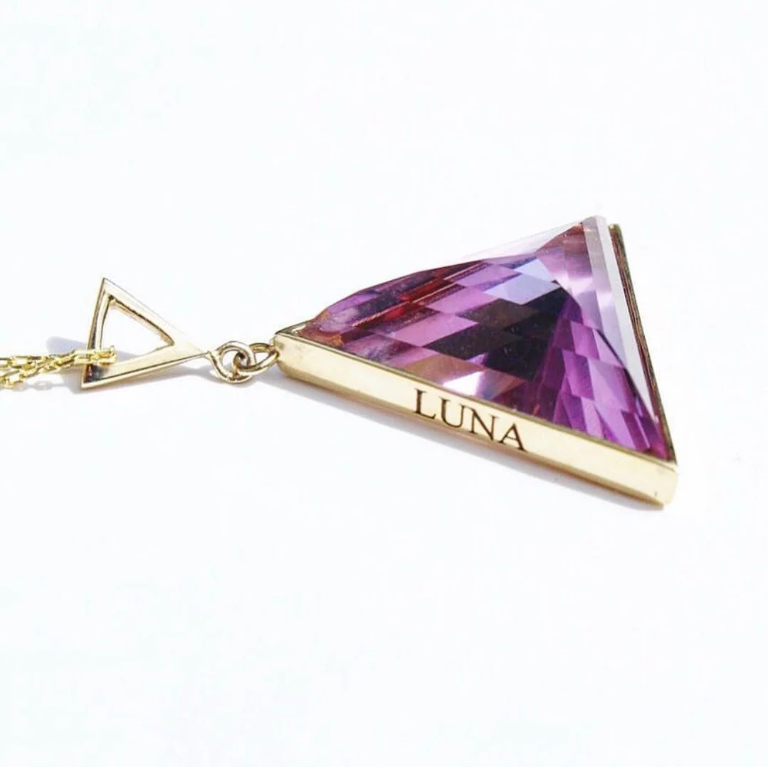 Gold necklace with a large, triangular, purple gemstone pendant engraved with the name "LUNA" on the side.