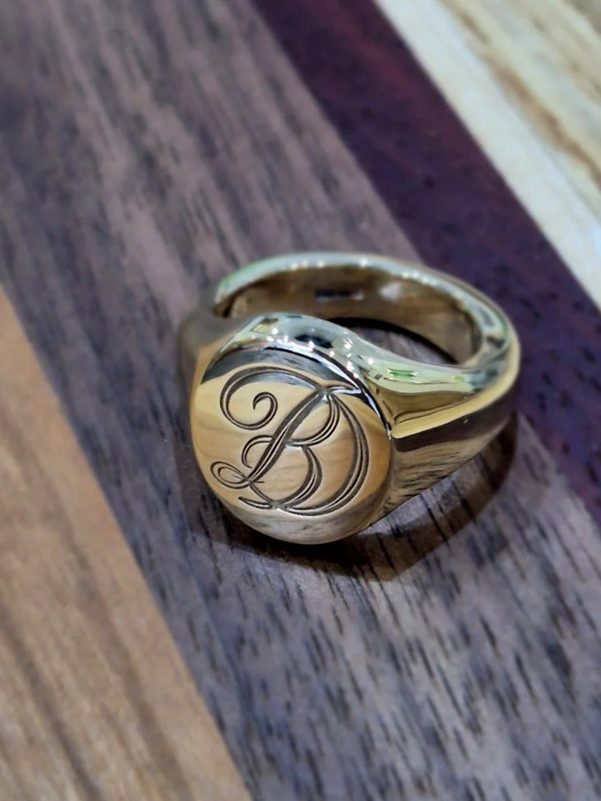 A gold signet ring with the letter 'B' engraved in a cursive font.