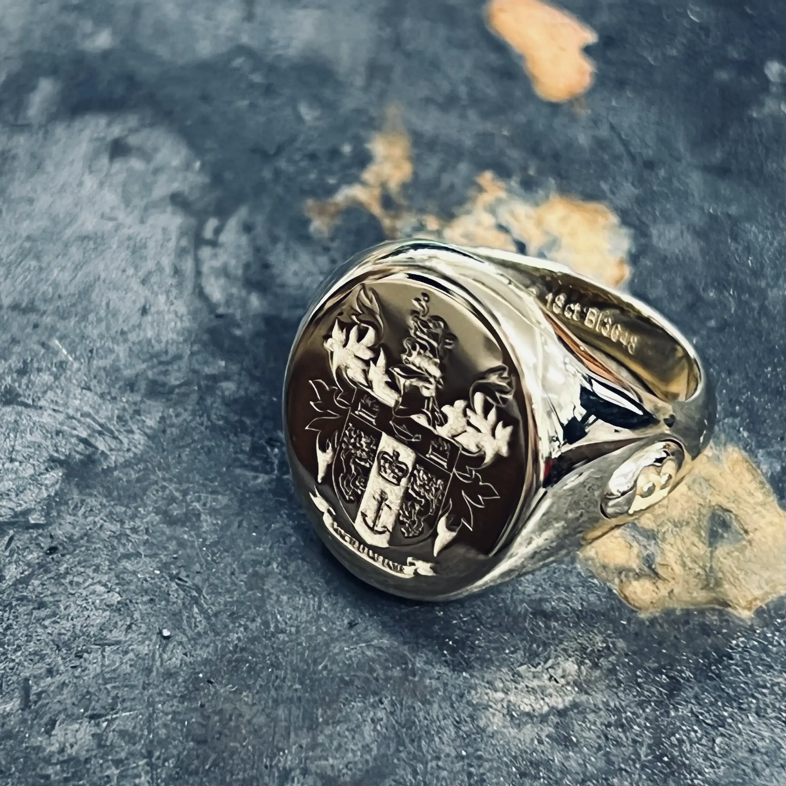 A close-up of a gold signet ring featuring a complex heraldic crest produced using precision laser technology. The laser carves deep into the metal to create an incredibly crisp finish, where the sharp, high-relief details stand out clearly against t