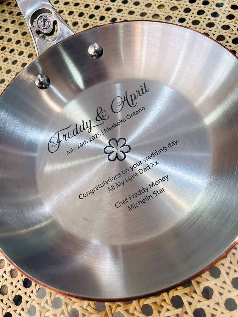 A silver frying pan with engraved custom text for a wedding, including names, date, and a message.