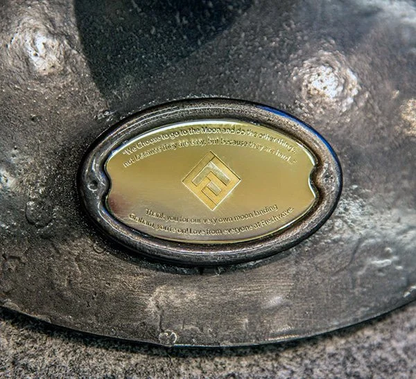 A brass metal plaque engraved with a logo and text underneath that has been embedded into the base of a trophy.
