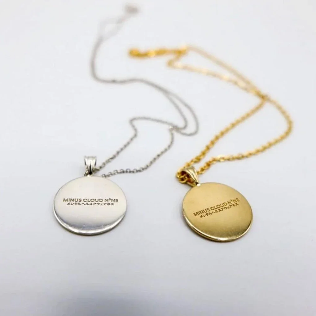 Two round pendant necklaces, one silver and one gold, with engraved text, lying on a white surface.
