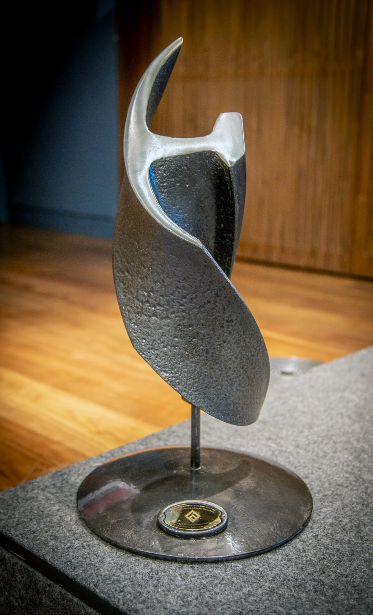 Engraved abstract trophy with curved, layered black and silver metal pieces on a round base.