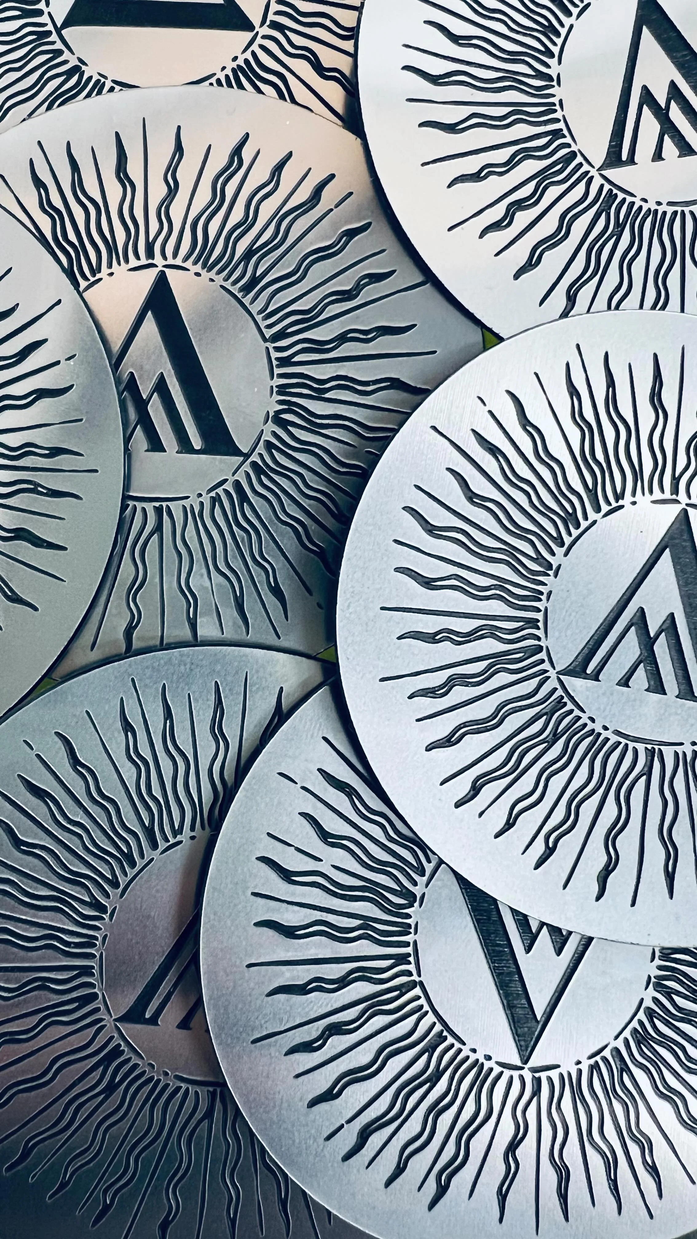 Close-up of multiple dual-tone acrylic badges engraved with a black sunburst design and a stylised 'M' logo in the centre.