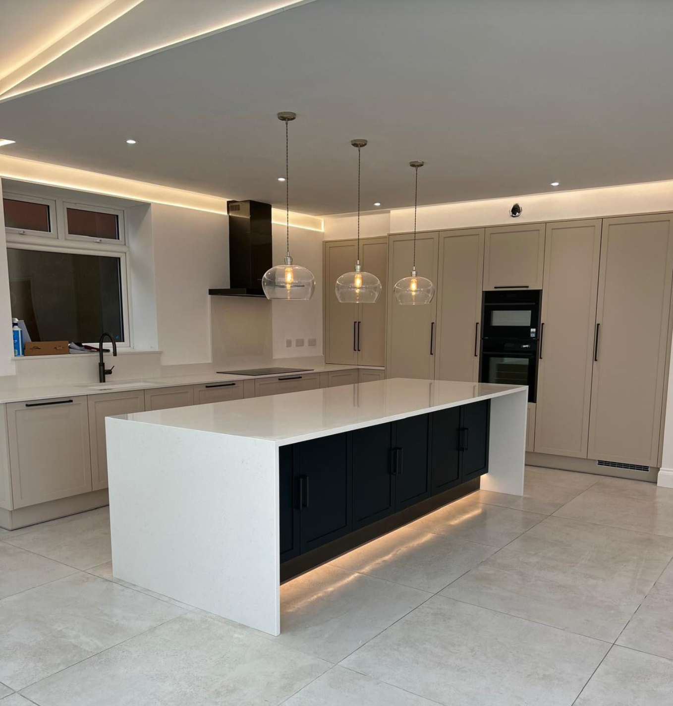 Modern kitchen with white and black cabinetry, a large white island, pendant lights, tiled floor, and a window above the sink.