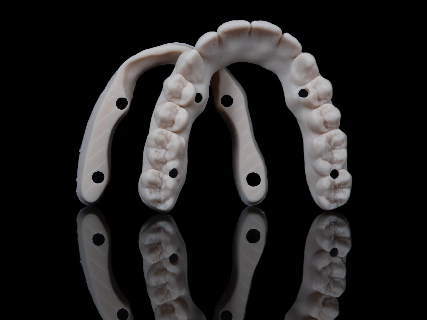 A dental implant surgical guide with multiple holes, placed on a reflective black surface with a mirrored reflection.